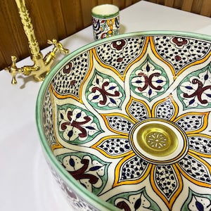 May include: A ceramic sink with a green, yellow, blue, and red floral pattern. The sink has a gold drain.