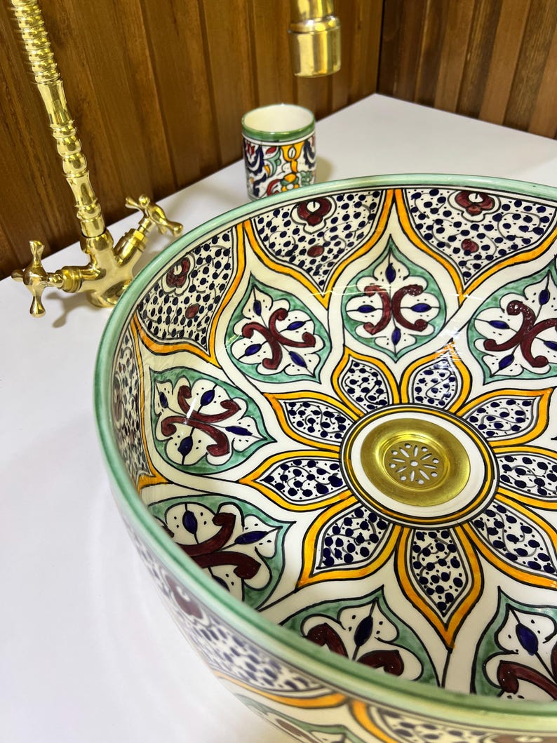 May include: A ceramic sink with a green, yellow, blue, and red floral pattern. The sink has a gold drain.