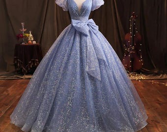 May include: A light blue tulle ball gown with a sweetheart neckline and short puff sleeves. The dress features a large bow at the waist and is adorned with silver glitter.