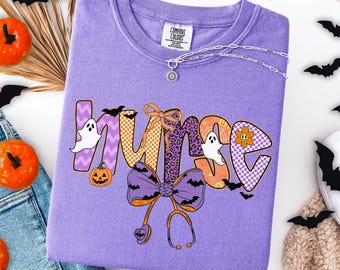 May include: A lavender Comfort Colors sweatshirt with a Halloween-themed "NURSE" graphic. The design includes ghosts, bats, pumpkins, and a stethoscope. The letters have various patterns, including checkered, leopard print, and zig-zag.