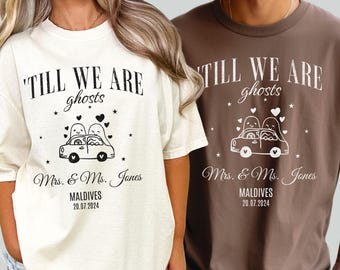 Może przedstawiać: Dwie koszulki, jedna kremowa i jedna brązowa, z napisem "TILL WE ARE ghosts" nad grafiką samochodu z dwiema postaciami duchów. Poniżej napis "Mrs. & Ms. Jones, MALDIVES 20.07.2024".