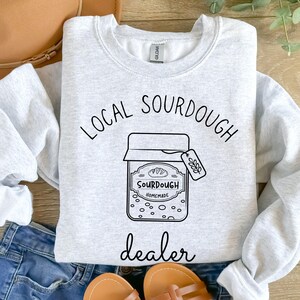 May include: Gray sweatshirt with the text "Local Sourdough Dealer" and a black and white illustration of a jar of sourdough bread.