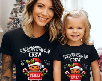 May include: Matching black t-shirts with the text "CHRISTMAS CREW" in white. Each shirt features a gingerbread man wearing a Santa hat and holding a sign with a name. One shirt says "EMMA" and the other says "EMILY".