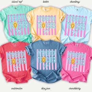 May include: A collection of short-sleeved t-shirts in various colors, including light green, yellow, light blue, red, blue, and pink. Each shirt features the text "INTERVENTION TEACHER" in a playful font, with a smiley face and bow graphic.