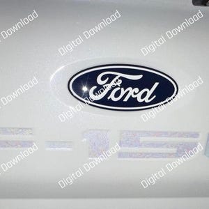 Puede incluir: Superficie blanca de vehículo con el logotipo de Ford en un óvalo azul y la palabra "Ford" en escritura blanca. Debajo del logo, las letras "F-150" son visibles en color claro.