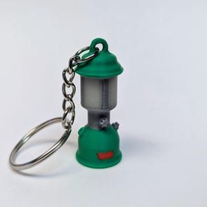 May include: A green and gray camping lantern keychain. The lantern has a metal chain and a silver ring.