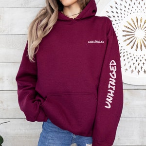 May include: Burgundy hoodie with the word "UNHINGED" printed on the front and the same word printed vertically on the left sleeve.