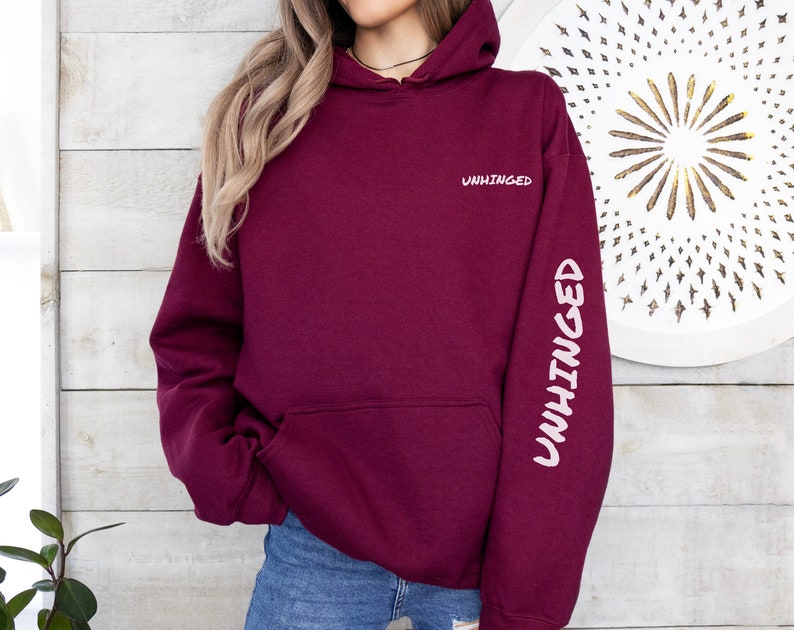 May include: Burgundy hoodie with the word "UNHINGED" printed on the front and the same word printed vertically on the left sleeve.