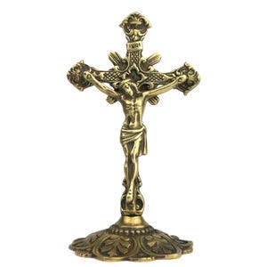 May include: An ornate brass crucifix depicting Jesus Christ. The cross features intricate detailing and stands on a round, floral-patterned base. The inscription "INRI" is visible at the top of the cross.