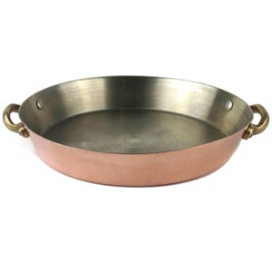 Puede incluir: Una sartén redonda de color cobre con un asa de latón a cada lado. El interior es de color plateado. La sartén está diseñada para cocinar y tiene un aspecto clásico y elegante. La sartén tiene aproximadamente 25 cm de diámetro.