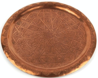 May include: A round copper serving tray with an intricate geometric design. The tray has a raised rim and a hammered finish.