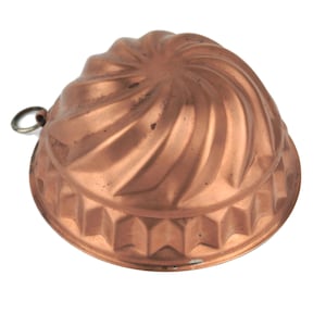 Puede incluir: Un molde para bizcocho de color cobre con un diseño en espiral en la parte superior y un patrón geométrico alrededor de la base. Tiene un pequeño anillo de metal para colgar. Utensilio de cocina vintage.
