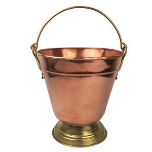 Puede incluir: Un cubo de cobre con asa y base de latón. El cubo es de diseño tradicional con fondo redondeado y parte superior acampanada.