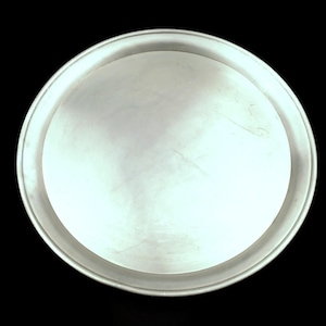 Peut inclure: Un plateau rond en métal argenté avec un bord légèrement surélevé. Le plateau a une surface lisse et réfléchissante sur un fond noir. Le design est simple et minimaliste.