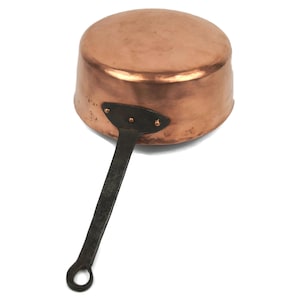 Peut inclure: Une casserole en cuivre avec une poignée en fer noir. La casserole a une finition martelée et un fond arrondi.