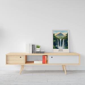 May include: A light wood media console with two drawers and open shelving. The console has a white top and is decorated with a framed print of a waterfall in Java, Indonesia. The print has the text "JAVA INDONESIA" below the image.
