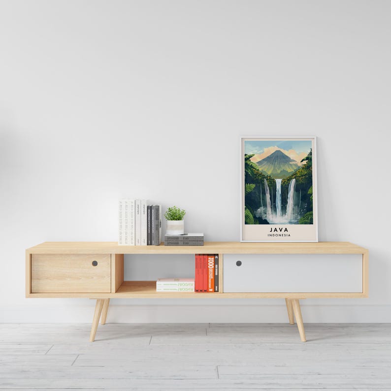 May include: A light wood media console with two drawers and open shelving. The console has a white top and is decorated with a framed print of a waterfall in Java, Indonesia. The print has the text "JAVA INDONESIA" below the image.