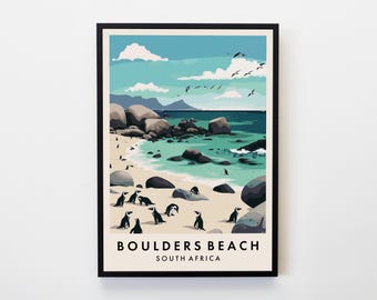 May include: A framed art print featuring a beach scene with penguins. The artwork depicts a turquoise ocean, sandy beach, and large rocks. The sky is light blue with white clouds and birds. The text "BOULDERS BEACH SOUTH AFRICA" is at the bottom.