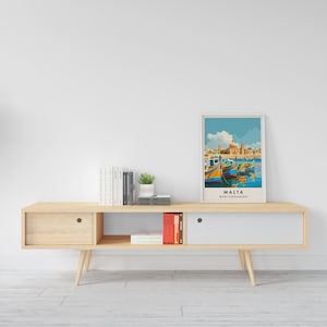 May include: A light wood media console with two drawers and an open shelf. The console has a white top and is decorated with a framed print of a colorful scene of boats in a harbor with the text "MALTA MEDITERRANEAN".