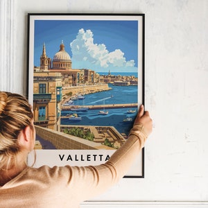 May include: A framed print of a colorful illustration of Valletta, Malta. The illustration shows a cityscape with a large church building, a harbor with boats, and a blue sky with white clouds. The print is hanging on a white wall.