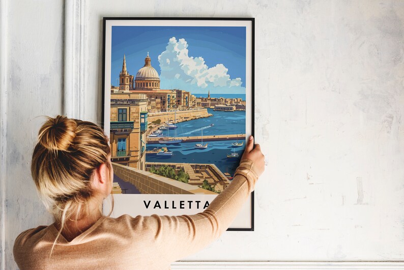 May include: A framed print of a colorful illustration of Valletta, Malta. The illustration shows a cityscape with a large church building, a harbor with boats, and a blue sky with white clouds. The print is hanging on a white wall.