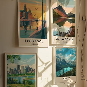 May include: Four framed travel posters with colorful illustrations of cityscapes and landscapes. The posters feature the cities of Liverpool, England, Snowdonia, Wales, Montreal, Canada, and Banff, Canada.