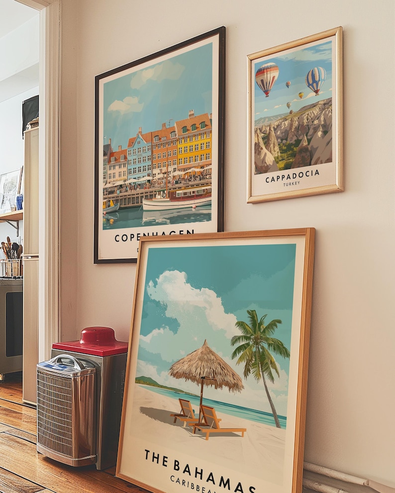 May include: Three framed travel posters on a white wall. The poster on the left shows a colorful cityscape with the text "Copenhagen" at the bottom. The poster in the middle shows a beach scene with a palm tree and a thatched umbrella. The text at the bottom reads "The Bahamas, Caribbean". The poster on the right shows a hot air balloon scene with the text "Cappadocia, Turkey".