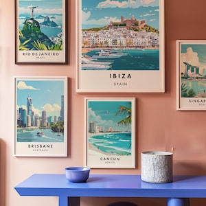 May include: Five framed travel posters with cityscapes and text below each image. The posters are hanging on a light pink wall. The posters are for Rio de Janeiro, Brazil; Ibiza, Spain; Brisbane, Australia; Cancun, Mexico; and Singapore, Asia. A blue table with a curved base is in the foreground.