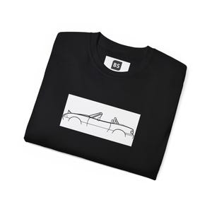 Puede incluir: Camiseta negra con un contorno blanco de un coche descapotable en la parte delantera. La camiseta tiene una pequeña etiqueta blanca con las letras "BS" en ella.