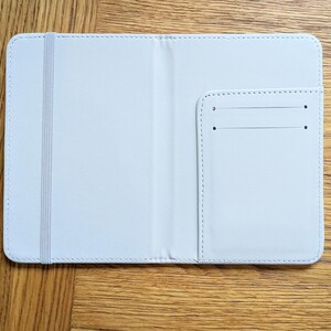 Pu&ograve; includere: Un portapassaporto in pelle bianca con una piccola tasca sul lato destro. Il portapassaporto ha un elastico bianco.