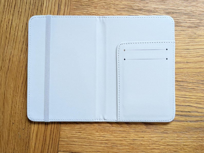Pu&ograve; includere: Un portapassaporto in pelle bianca con una piccola tasca sul lato destro. Il portapassaporto ha un elastico bianco.