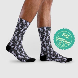 Może przedstawiać: Para czarnych skarpet z białym i szarym wzorem abstrakcyjnych kształtów i linii. Skarpety są pokazane na nogach modelki. Tekst "DARMOWA DOSTAWA" znajduje się w zielonym kółku z białą ikoną ciężarówki.