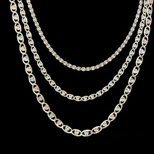 May include: Three gold chains with heart-shaped links. The chains are layered, with the largest chain on the bottom and the smallest chain on top. The chains are made of yellow, white, and rose gold.