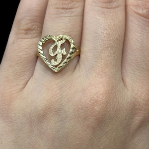 May include: A gold heart-shaped ring with a cursive letter "F" inside the heart.