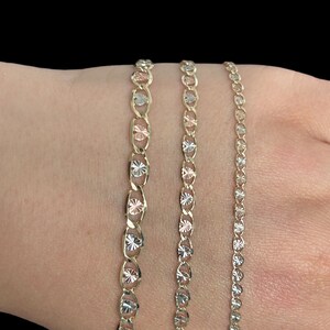 Puede incluir: Tres cadenas de oro con un dise&ntilde;o de corte de diamante. Las cadenas est&aacute;n superpuestas y tienen diferentes longitudes. La cadena de abajo es la m&aacute;s larga y la cadena de arriba es la m&aacute;s corta.