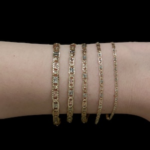 K&ouml;nnte beinhalten: Vier goldene Ketten in verschiedenen L&auml;ngen und Breiten mit einem strukturierten Design werden auf dem Arm einer Person gezeigt.