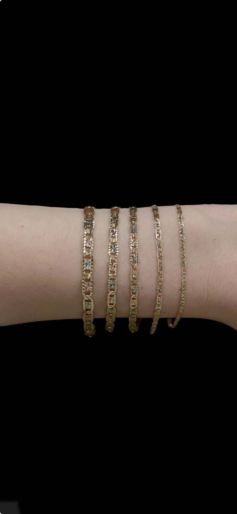 K&ouml;nnte beinhalten: Vier goldene Ketten in verschiedenen L&auml;ngen und Breiten mit einem strukturierten Design werden auf dem Arm einer Person gezeigt.