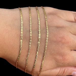 Pu&ograve; includere: Quattro collane a catena color oro con un design a maglie da marinaio sono esposte su una mano su sfondo nero. Le catene sono sottili e hanno una finitura lucida, che riflette la luce.