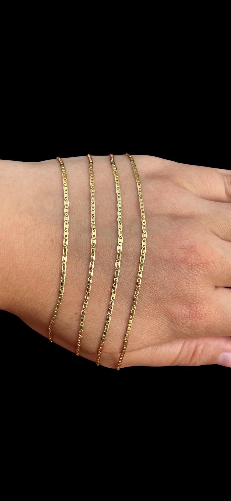 Pu&ograve; includere: Quattro collane a catena color oro con un design a maglie da marinaio sono esposte su una mano su sfondo nero. Le catene sono sottili e hanno una finitura lucida, che riflette la luce.