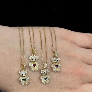 Pode incluir: Quatro colares de ouro com um pingente de urso de pelúcia. Cada pingente é adornado com pedras transparentes brilhantes e uma pedra em forma de coração no centro. Os corações são vermelhos, verdes, vermelhos e verdes.