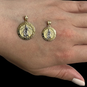 May include: Two gold pendants with a saint image and the words "Saint Lazarus Pray For Us" on a hand.