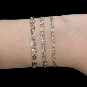 Puede incluir: Tres pulseras de oro con un patr&oacute;n de diamante en la mu&ntilde;eca de una persona. Las pulseras tienen diferentes anchos.
