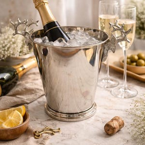 May include: A silver champagne bucket with ice holds a bottle of champagne. The bucket has deer antler handles. Two champagne flutes and a cork are also visible, suggesting a celebratory theme.