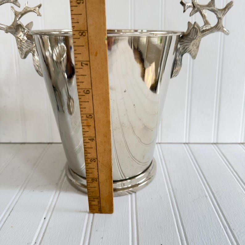 May include: A silver-colored metal wine bucket with deer antler handles. The bucket is approximately 8 inches tall and has a round base. The handles are detailed with a realistic antler design.