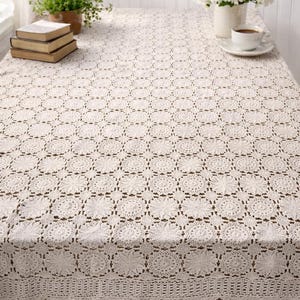 May include: A white ceramic mug with a black handle and the text "But First, Coffee" in a bold, black font. The mug is set against a blurred background, suggesting a cozy setting.