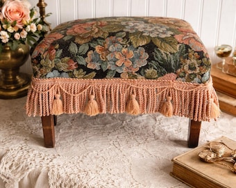Taburete de madera vintage con tela floral y borlas.