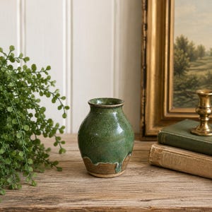 May include: A small ceramic vase with a rounded body and a narrow neck. The upper portion features a speckled forest green glaze that drips down over a solid, earthy brown base. The surface has a glossy finish with visible texture.