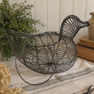 May include: A dark gray wire basket shaped like a duck, featuring a rounded body, a curved neck, and a head with a defined beak. The basket is constructed from thin, interconnected metal wire, creating an open, cage-like structure with a handle.