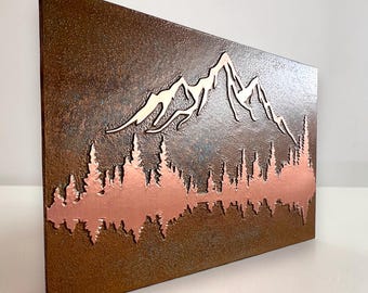 May include: A rectangular metal wall art piece featuring a textured, rusted brown finish. The design includes a metallic silver mountain range silhouette at the top and a copper-colored forest line at the bottom, creating a layered landscape.