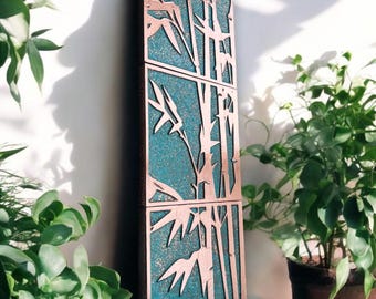 May include: A copper-colored wall art piece with a design of bamboo stalks and leaves. The piece is made of three panels and has a textured, turquoise-colored background.